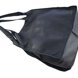 May include: A black leather tote bag with a single strap. The bag has a large, open top and a flap that can be folded over to close the bag.