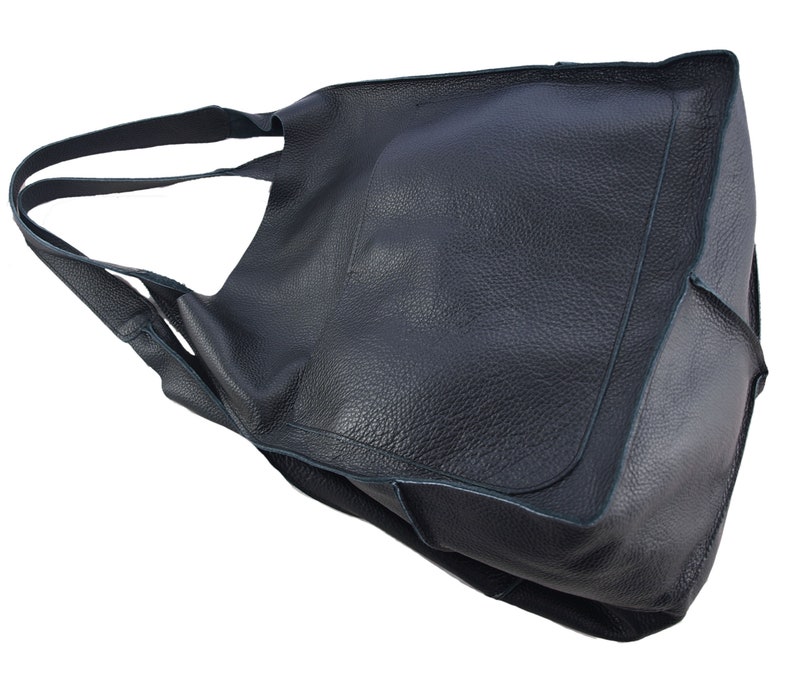 May include: A black leather tote bag with a single strap. The bag has a large, open top and a flap that can be folded over to close the bag.