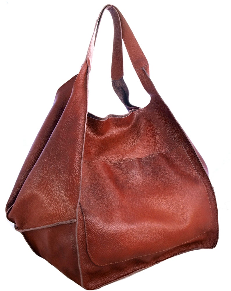 Puede incluir: Un bolso tote de cuero marr&oacute;n con un bolsillo &uacute;nico en la parte delantera. El bolso tiene una parte superior ancha y abierta y dos correas largas.