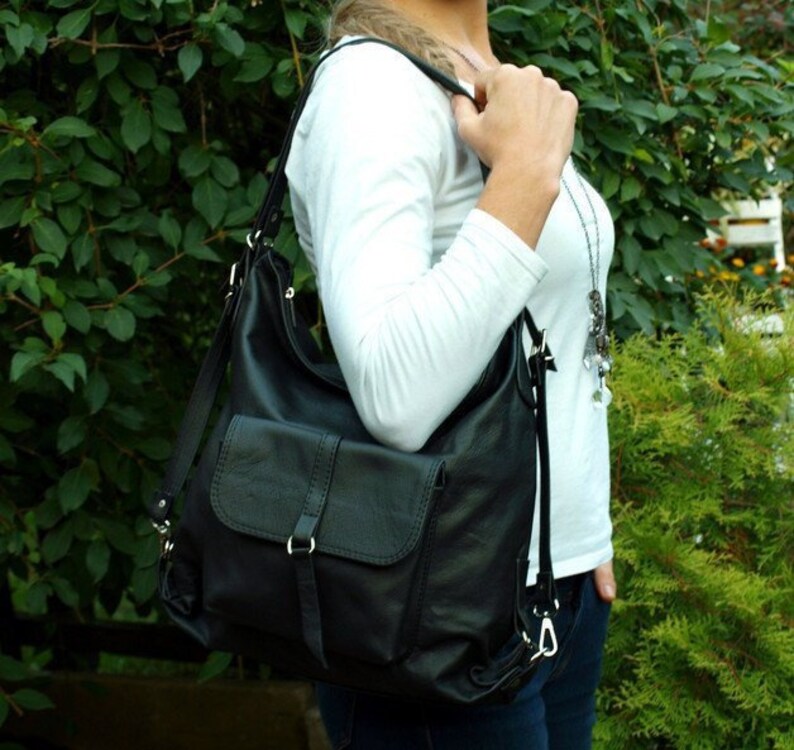 May include: Black leather shoulder bag with a flap pocket and adjustable strap. The bag is worn over the shoulder, showcasing its design and functionality. The bag has silver hardware and a buckle closure.