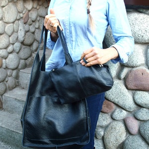 May include: A black leather tote bag with a smaller black leather pouch attached to the front. The bag has a top zipper closure and a long strap.