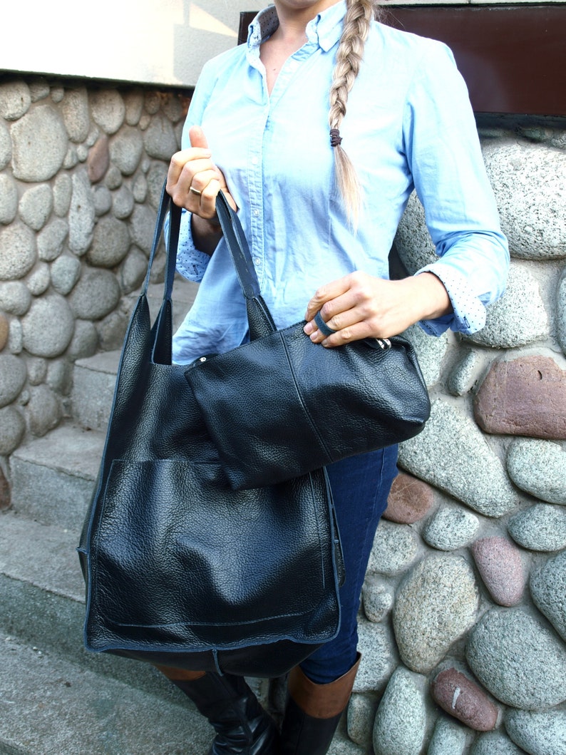 May include: A black leather tote bag with a smaller black leather pouch attached to the front. The bag has a top zipper closure and a long strap.