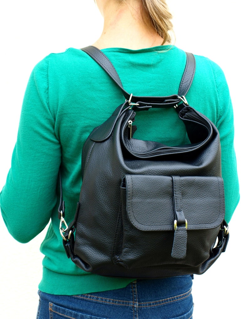 May include: Black leather backpack with a flap pocket and adjustable straps. The backpack has a zippered main compartment and a top handle. The leather has a textured appearance. The hardware is silver-colored.