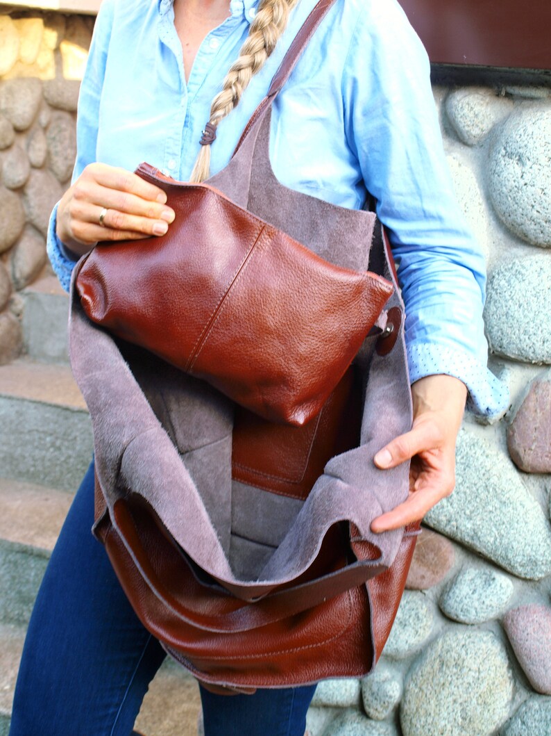 Puede incluir: Un bolso tote de cuero marr&oacute;n con un bolsillo con cremallera en el interior. El bolso est&aacute; abierto y el forro es visible. El forro es de color gris claro.