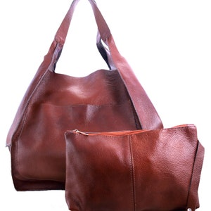 Puede incluir: Un bolso tote de cuero marr&oacute;n con una bolsa de cuero marr&oacute;n a juego. El bolso tote tiene una parte superior grande y abierta y dos asas largas. La bolsa tiene una cremallera y una correa peque&ntilde;a.