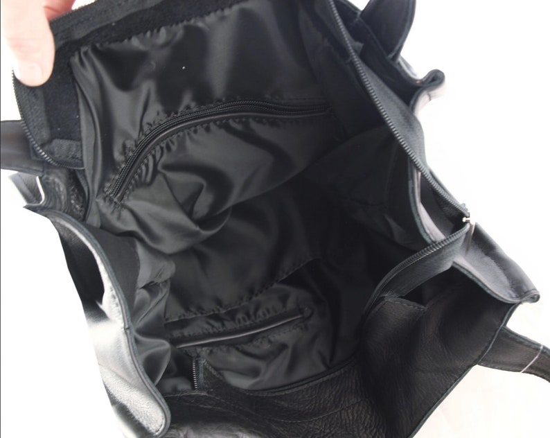 May include: Black leather tote bag with an open interior. The bag features a zippered pocket and a black fabric lining. The top of the bag has a velcro closure. The bag has two handles.