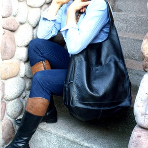 May include: A woman wearing blue jeans and brown leather boots sits on a stone staircase with a large black leather tote bag.