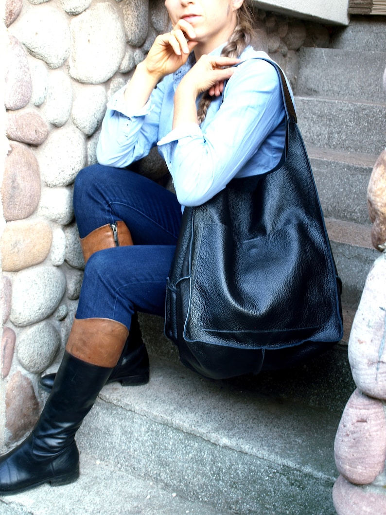 May include: A woman wearing blue jeans and brown leather boots sits on a stone staircase with a large black leather tote bag.