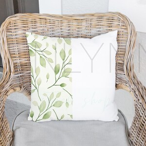 May include: A white wicker chair with a gray cushion and a pillow with a green leafy pattern on one side and the text "& lovely" on the other side.