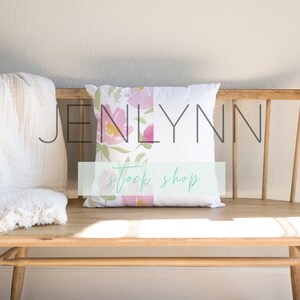 May include: A white throw blanket with fringed edges is draped over a wooden bench. A white cushion with a floral pattern is on the bench. The cushion has the text "Jenlynn Stock Shop" printed on it.