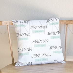 May include: White pillow with a repeating pattern of the text "Jenlynn Shop" in black lettering on a white background. The pillow is sitting on a wooden bench.