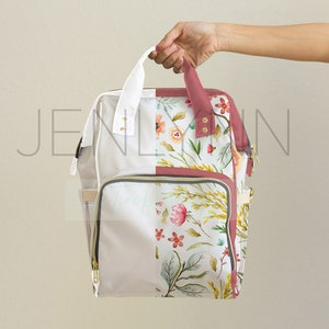 May include: A floral print backpack with a white handle and a white and floral design. The backpack has a front pocket with a gold zipper and a side pocket. The floral design includes pink and yellow flowers and green leaves.