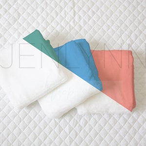 May include: Three white folded towels on a white quilted surface. The towels are arranged in a triangle shape with the top towel folded in half and the bottom two towels folded in thirds. The towels are surrounded by a teal, blue, and coral colored background.