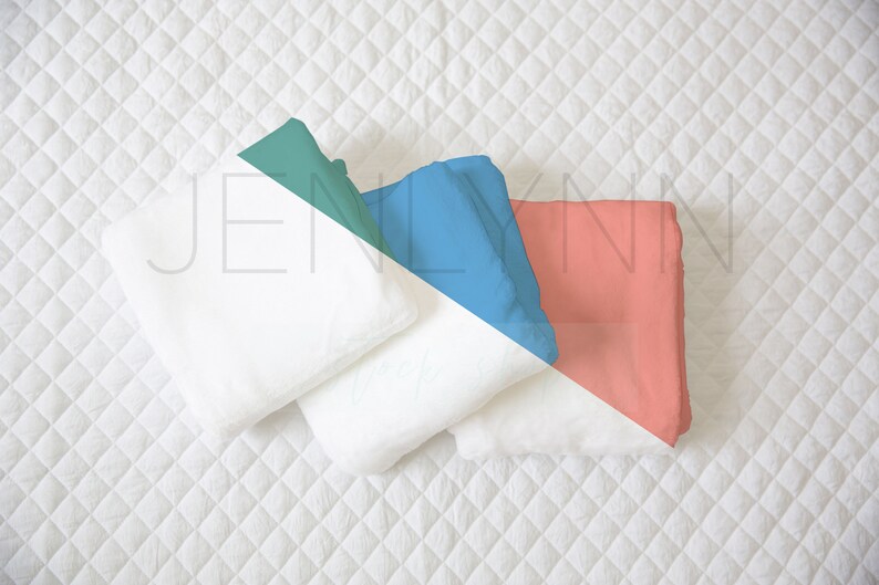 May include: Three white folded towels on a white quilted surface. The towels are arranged in a triangle shape with the top towel folded in half and the bottom two towels folded in thirds. The towels are surrounded by a teal, blue, and coral colored background.