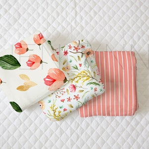 May include: Three fabric swatches with floral patterns. The first swatch features pink flowers and green leaves on a white background. The second swatch has a more detailed floral pattern with pink, yellow, and green flowers and leaves on a white background. The third swatch is a pink and white striped fabric.