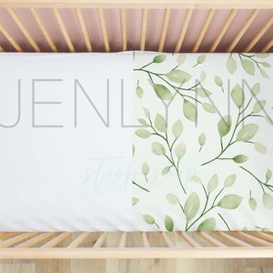 May include: A white crib sheet with a green leafy pattern on one side. The sheet is fitted and has elastic around the edges. The crib sheet is made of soft, breathable fabric.