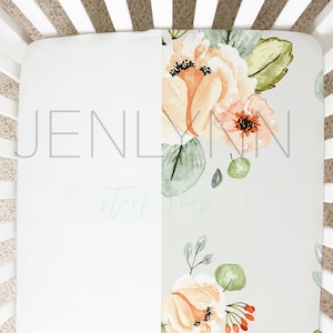 May include: A fitted crib sheet with a floral pattern featuring peach and green watercolor flowers on a light gray background. The sheet is tucked into a white crib.