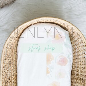 May include: A woven wicker basket with a white fitted sheet with a floral pattern. The sheet has the text "Jenlyni Stock Shop" printed on it.