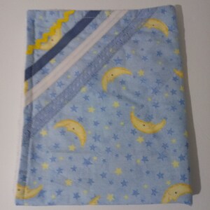 May include: A blue baby blanket with a yellow crescent moon and star pattern. The blanket has a white and blue trim with a yellow zig-zag pattern.