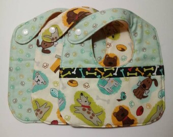 May include: Three baby bibs with a dog print. The bibs are green, white and yellow with a black and white bone pattern. The bibs have a snap closure.
