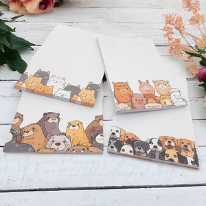 Könnte beinhalten: Drei verschiedene Designs von Notizblockpapier mit Tierillustrationen. Der erste Notizblock zeigt einen Rand mit verschiedenen Katzen, der zweite Notizblock zeigt einen Rand mit verschiedenen Hunden und der dritte Notizblock zeigt einen Rand mit verschiedenen Ottern.