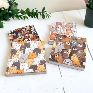Könnte beinhalten: Vier verschiedene Notizbücher mit Tiermotiven. Die Notizbücher zeigen Katzen, Hunde, Otter und eine Vielzahl anderer Tiere. Die Notizbücher sind alle gleich groß und haben einen weißen Hintergrund.