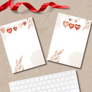 Könnte beinhalten: Zwei leere weiße Papierbögen mit Aquarell-Herzdekorationen und braunen Blattakzenten. Ein rotes Band und eine weiße Tastatur sind ebenfalls sichtbar. Die Herzen sind in Rot-, Rosa- und Beigetönen gehalten.