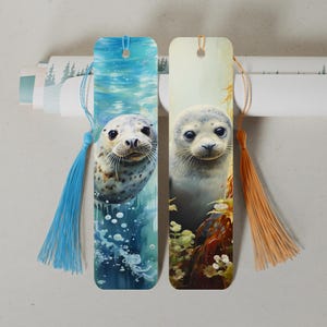 Könnte beinhalten: Zwei farbenfrohe Lesezeichen mit einer Nahaufnahme eines Seehundbabys. Ein Lesezeichen zeigt das Seehundbaby unter Wasser mit blauen und grünen Wasserfarben. Das andere Lesezeichen zeigt das Seehundbaby an Land mit braunen, grünen und weißen Farben.