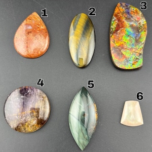 May include: Six polished gemstones labeled one through six. Number one is a teardrop-shaped orange stone. Two is an oval yellow and black striped stone. Three is an iridescent, multi-colored irregular stone. Four is a round purple and gold stone. Five is a green marquise-shaped stone. Six is a small, trapezoidal pale pink stone.