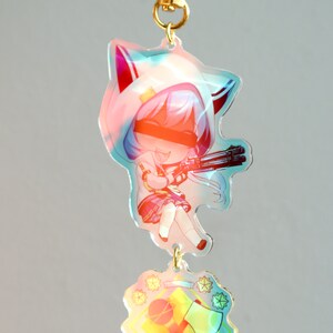 May include: A colorful anime character keychain with a white hooded jacket, blue hair, and a gun. The keychain also features a separate charm with a yellow background and a red axe and a baseball bat.