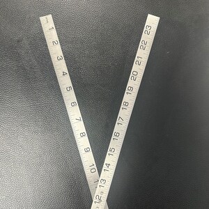May include: Two silver metal rulers, one with markings from 1 to 10 inches and the other from 12 to 23 inches, are positioned in a V shape.