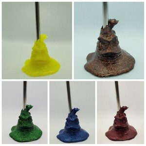 Peut inclure: Ensemble de cinq porte-crayons en forme de chapeau de tri, recouverts de paillettes de différentes couleurs. Chaque porte-crayon est d'une couleur différente : jaune, marron, vert, bleu et rouge.