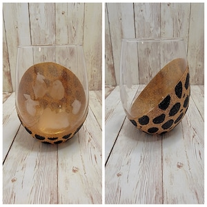 Puede incluir: Dos portavelas de vidrio transparente con un diseño de estampado animal en oro y negro. Los portavelas están vacíos y se encuentran sobre una superficie de madera.