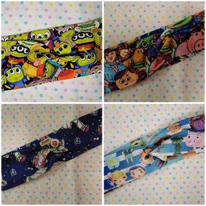 May include: Four different colorful fabric headbands with a knotted design. Each headband features a different pattern of characters from the Toy Story franchise, including Woody, Buzz Lightyear, Jessie, and the Aliens.