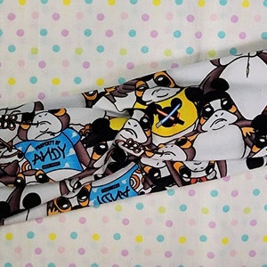 May include: A white headband with a repeating pattern of cartoon characters. The characters are wearing various outfits, including a blue shirt with the text "Property of Andy" and a red and white polka dot shirt.