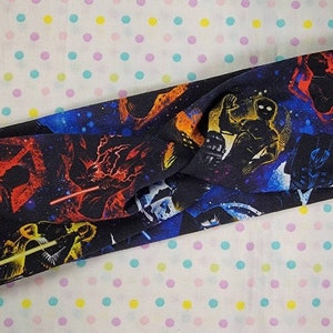 May include: A black headband with a galaxy print featuring characters from Star Wars. The characters are in silhouette and include Darth Vader, Luke Skywalker, and Yoda.