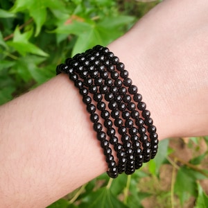May include: A black beaded bracelet with multiple strands of small, round beads. The bracelet is worn on a person's wrist.
