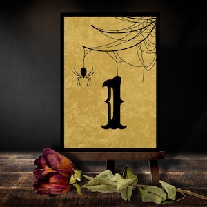 May include: A black and gold Halloween table number card with a spider and web design. The number one is displayed in a black gothic font.