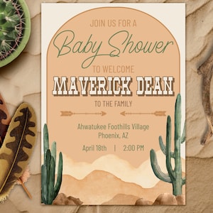 May include: A rectangular baby shower invitation card featuring a tan arch design, green text, and desert illustrations. The text reads: JOIN US FOR A Baby Shower TO WELCOME MAVERICK DEAN TO THE FAMILY, Ahwatukee Foothills Village Phoenix, AZ, April 18th | 2:00 PM.