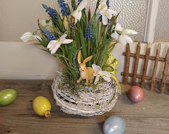 Composizione floreale a forma di nido di vite con bucaneve, muscari e una lepre