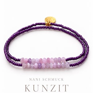 Puede incluir: Una pulsera de doble hilo con cuentas de color morado oscuro y una sección central de piedras preciosas de kunzita rosa claro facetadas. Un pequeño dije circular dorado está sujeto en la parte superior. El texto NANI SCHMUCK KUNZIT fein edel mauve es visible.