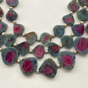 May include: A multi-strand necklace featuring irregular-shaped beads. The beads have a blue-green outer layer with a vibrant magenta center. Small silver-colored beads separate each stone. The necklace is displayed against a white background.
