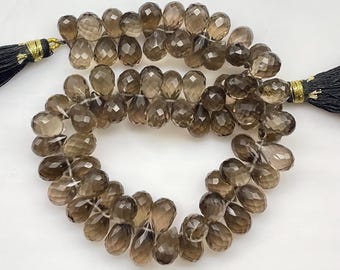 May include: A strand of faceted, teardrop-shaped smoky quartz beads in a translucent brown hue. The beads are arranged in a circular formation and are secured at both ends by black thread tassels with gold-colored metallic thread accents.