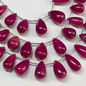May include: A strand of ruby red gemstone beads in a teardrop shape. The beads are strung on silver wire.