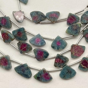 May include: Strands of gemstone beads. Each bead is a triangular shape with a blue-green hue and a central splash of deep pink. The beads are strung on a silver-colored wire, creating a necklace or bracelet.