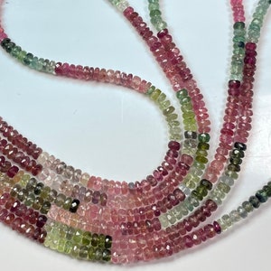 May include: A strand of multi-coloured tourmaline beads. The beads are faceted and have a variety of shades of pink, green, and black.