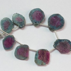 May include: A strand of eight faceted, round, blue and pink gemstone beads strung on silver wire. The beads are approximately 1.5 cm in diameter.