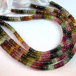 May include: Multicoloured Tourmaline gemstone beads in a range of shades of green, pink, brown, and black. The beads are faceted and have a slightly rounded shape. The beads are strung on a white thread and are ready to be used for jewellery making.