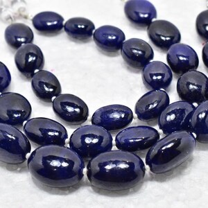 Puede incluir: Una hebra de cuentas de piedras preciosas ovaladas de color azul oscuro. Las cuentas están enhebradas en un cordón blanco y tienen un acabado pulido.