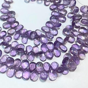 Puede incluir: Una hebra de cuentas de piedra preciosa de amatista de color púrpura claro en forma de pera. Las cuentas son facetadas y tienen un acabado liso y pulido.